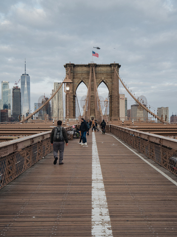 View of Brooklyn Bridge with pedestrians walking on the wooden path suspension cables and the Manhattan skyline in the background. New York New York United States.