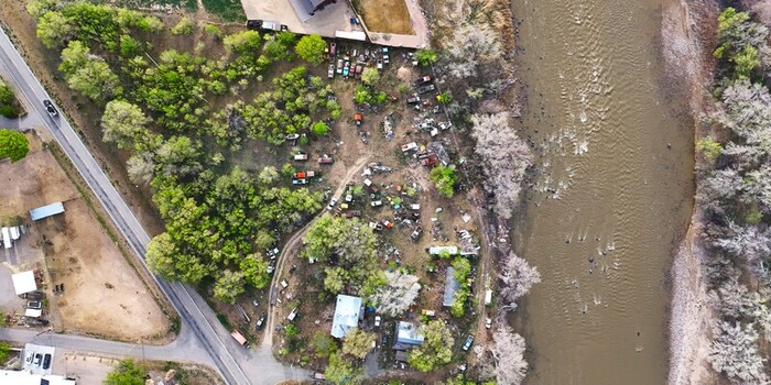 Aerial view of a river flowing with a collection of old cars nestled among verdant trees on its banks contrasting with the muddy waters Palisade Colorado USA. Aerial view of a river flowing with a collection of old cars nestled among verdant trees on its banks contrasting with the muddy waters Palisade Colorado USA.
