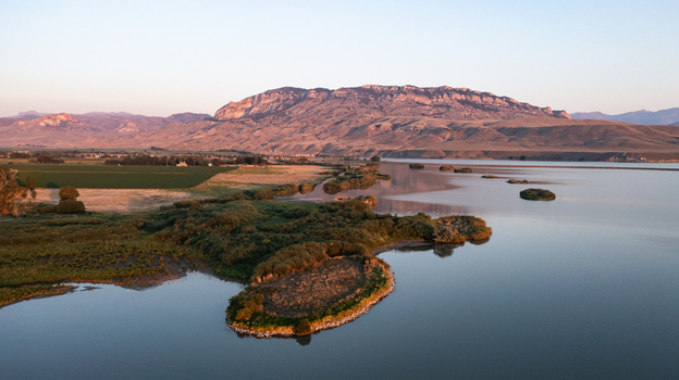 Aerial view of the landscape near Cody featuring a calm lake lush green vegetation along the shoreline and distant mountains under a clear sky in Cody Wyoming United States.