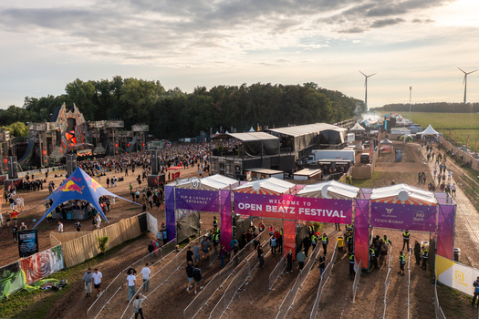 Herzogenaurach Germany 27 July 2025 Aerial view of Open Beatz Festival with crowds entering through the main gate stages and wind turbines under a sunset sky. Herzogenaurach Germany 27 July 2025 Aerial view of Open Beatz Festival with crowds entering through the main gate stages and wind turbines under a sunset sky.