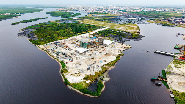 Aerial view of a large construction site in Satellite Town featuring industrial buildings cranes and raw materials surrounded by the lagoon in Lagos Lagos Nigeria.