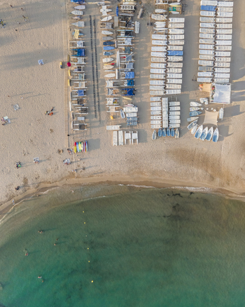 Aerial view of small boats parked in neat rows on a sandy beach next to turquoise sea water with swimmers in Sitges Catalonia Spain. Aerial view of small boats parked in neat rows on a sandy beach next to turquoise sea water with swimmers in Sitges Catalonia Spain.