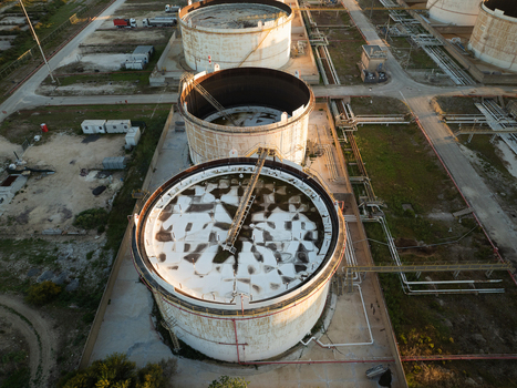 Aerial view of large industrial storage tanks with floating roofs and complex piping systems at an oil refinery in Augusta Sicily Italy. Aerial view of large industrial storage tanks with floating roofs and complex piping systems at an oil refinery in Augusta Sicily Italy.