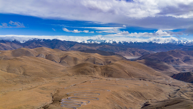 Aerial view of Gawula pass featuring a winding mountain road snaking through the arid landscape of the Himalayas with snow capped peaks in Shigatse Tibet China.