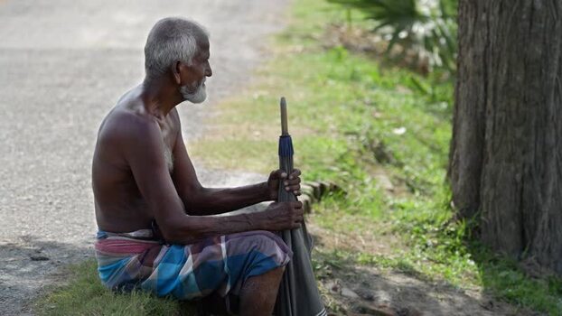 View of an elderly man sitting by a road with an umbrella Bangladesh. View of an elderly man sitting by a road with an umbrella Bangladesh.
