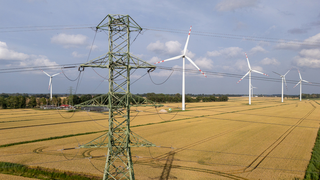Aerial view of wind turbines in a golden wheat field with a large electricity pylon in the foreground under a blue sky in Gdansk Pomeranian Voivodeship Poland. Aerial view of wind turbines in a golden wheat field with a large electricity pylon in the foreground under a blue sky in Gdansk Pomeranian Voivodeship Poland.