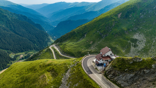 Aerial view of the Transfagarasan road winding through the lush green Carpathian Mountains with a mountain lodge perched on the edge in Curtea de Arges Judetul Arges Romania.
