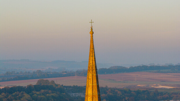 Aerial view of the spire of Salisbury Cathedral illuminated by golden hour light rising above the rolling countryside of Salisbury England United Kingdom. Aerial view of the spire of Salisbury Cathedral illuminated by golden hour light rising above the rolling countryside of Salisbury England United Kingdom.
