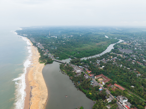 Aerial view of the coastline featuring a sandy beach a river mouth with a bridge and lush tropical greenery under an overcast sky Galle Southern Province Sri Lanka. Aerial view of the coastline featuring a sandy beach a river mouth with a bridge and lush tropical greenery under an overcast sky Galle Southern Province Sri Lanka.