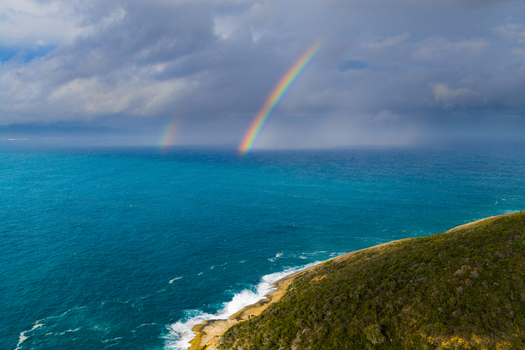 Aerial view of a double rainbow over the turquoise waters of Two Peoples Bay Nature Reserve with crashing waves against the green coastline in Albany Western Australia Australia.