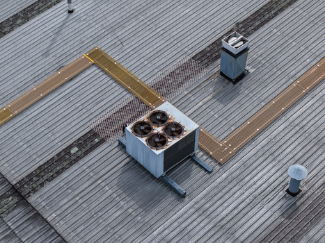 Aerial view of an industrial HVAC unit with four fans mounted on a corrugated metal roof with metal walkways and ventilation pipes in Melbourne VIC Australia.