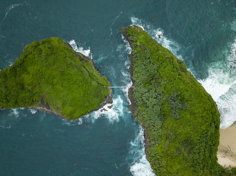 Aerial view of lush green cliffs connected by a bridge amidst the turquoise sea at Sedahan Beach Gunungkidul Regency Special Region of Yogyakarta Indonesia. Aerial view of lush green cliffs connected by a bridge amidst the turquoise sea at Sedahan Beach Gunungkidul Regency Special Region of Yogyakarta Indonesia.