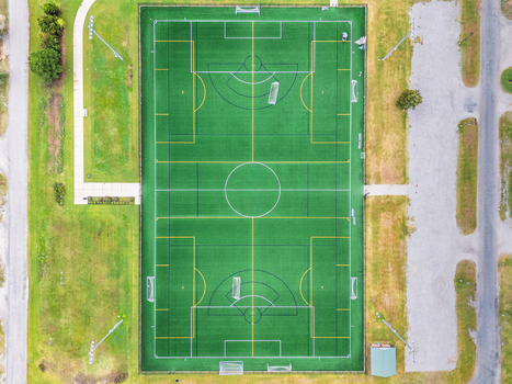 Aerial view of nCino Sports Park featuring a green synthetic turf soccer field with white and yellow markings surrounded by grass and parking areas in Wilmington North Carolina United States. Aerial view of nCino Sports Park featuring a green synthetic turf soccer field with white and yellow markings surrounded by grass and parking areas in Wilmington North Carolina United States.