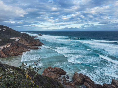 View of the rugged coastline with turquoise waves crashing against rocky cliffs under a cloudy sky in Plettenberg Bay Western Cape South Africa. View of the rugged coastline with turquoise waves crashing against rocky cliffs under a cloudy sky in Plettenberg Bay Western Cape South Africa.
