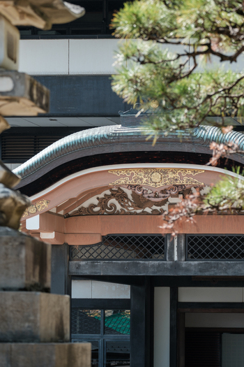 View of intricate golden details adorning the curved eaves of a traditional Japanese building framed by the textured stone of a lantern Narita Chiba Japan. View of intricate golden details adorning the curved eaves of a traditional Japanese building framed by the textured stone of a lantern Narita Chiba Japan.