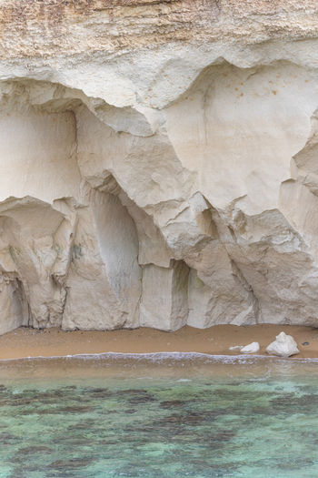 View of white limestone cliffs overlooking a small sandy beach and clear turquoise water Syracuse Sicily Italy.