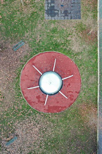 Aerial view of a circular climbing structure on a red rubber surface surrounded by green grass and fallen leaves in a park in Turin Piedmont Italy. Aerial view of a circular climbing structure on a red rubber surface surrounded by green grass and fallen leaves in a park in Turin Piedmont Italy.