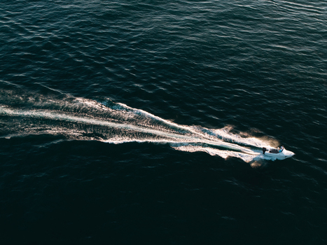 Aerial view of a small motorboat cruising across the dark blue ocean leaving a bright white wake behind it in Dee Why New South Wales Australia. Aerial view of a small motorboat cruising across the dark blue ocean leaving a bright white wake behind it in Dee Why New South Wales Australia.