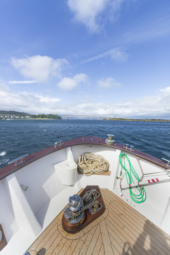 View of the Skye Bridge seen from the bow of a boat on the water with a coiled rope and anchor on the deck under a blue sky in Isle of Skye United Kingdom. View of the Skye Bridge seen from the bow of a boat on the water with a coiled rope and anchor on the deck under a blue sky in Isle of Skye United Kingdom.