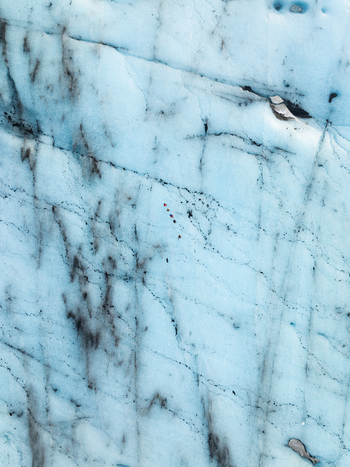 Aerial view of Breidamerkurjokull glacier with deep blue ice dark ash streaks and a small group of hikers walking on the surface in Sveitarfelagid Hornafjordur Iceland. Aerial view of Breidamerkurjokull glacier with deep blue ice dark ash streaks and a small group of hikers walking on the surface in Sveitarfelagid Hornafjordur Iceland.