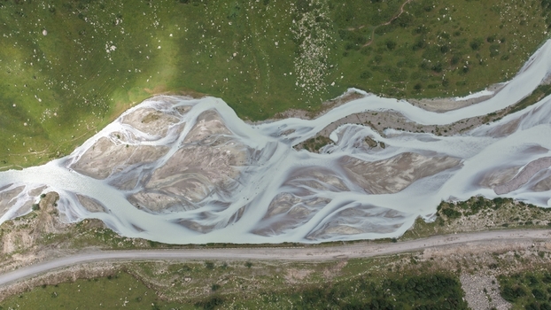 Aerial view of the braided Enilchek River with glacial meltwater light colored sediment lush green grassy banks and a dirt road in Enilchek Issyk Kul Region Kyrgyzstan. Aerial view of the braided Enilchek River with glacial meltwater light colored sediment lush green grassy banks and a dirt road in Enilchek Issyk Kul Region Kyrgyzstan.