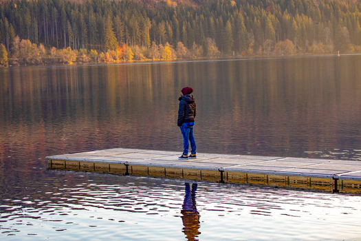 View of a person standing on a wooden pier overlooking a calm lake surrounded by an autumn forest with colorful trees Breitnau Baden Wurttemberg Germany. View of a person standing on a wooden pier overlooking a calm lake surrounded by an autumn forest with colorful trees Breitnau Baden Wurttemberg Germany.