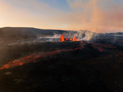 Aerial view of a volcanic eruption with glowing lava flows and smoke rising from the dark volcanic landscape under a twilight sky in Iceland. Aerial view of a volcanic eruption with glowing lava flows and smoke rising from the dark volcanic landscape under a twilight sky in Iceland.