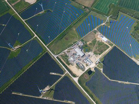 Aerial view of Chelveston Wind Farm featuring vast solar panel arrays and wind turbines casting long shadows over the green landscape in Wellingborough England United Kingdom. Aerial view of Chelveston Wind Farm featuring vast solar panel arrays and wind turbines casting long shadows over the green landscape in Wellingborough England United Kingdom.