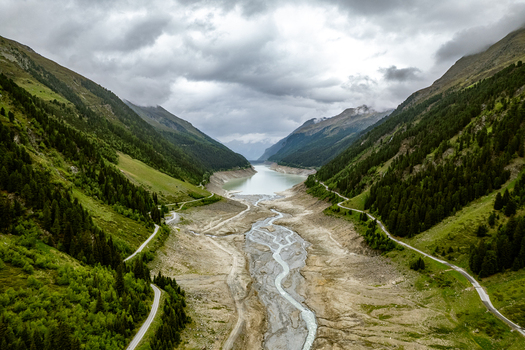 Aerial view of the mountain valley with a winding river flowing into a reservoir surrounded by lush green pine forests and steep slopes under a cloudy sky in Prutz Tyrol Austria. Aerial view of the mountain valley with a winding river flowing into a reservoir surrounded by lush green pine forests and steep slopes under a cloudy sky in Prutz Tyrol Austria.