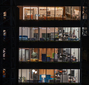 Aerial view of an illuminated modern office building at night with visible workspaces desks and interior lighting in New York New York United States. Aerial view of an illuminated modern office building at night with visible workspaces desks and interior lighting in New York New York United States.