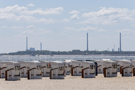 View of Strand Schillig with rows of numbered white hooded beach chairs on the sand and industrial chimneys on the horizon across the water in Wangerland Niedersachsen Germany. View of Strand Schillig with rows of numbered white hooded beach chairs on the sand and industrial chimneys on the horizon across the water in Wangerland Niedersachsen Germany.