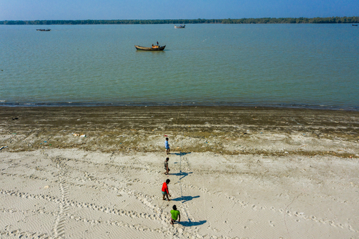 Aerial view of Kuakata beach with people walking on the sand towards the water and a small wooden boat floating in the sea Kuakata Barisal Division Bangladesh. Aerial view of Kuakata beach with people walking on the sand towards the water and a small wooden boat floating in the sea Kuakata Barisal Division Bangladesh.