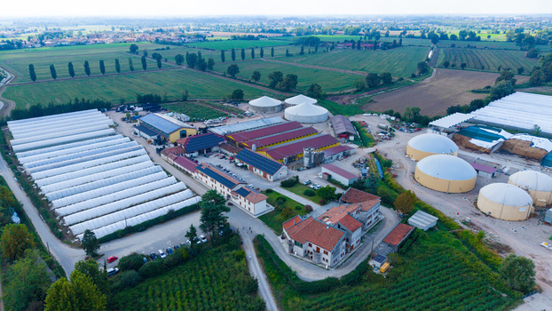 Aerial view of an Italian cattle farm featuring large greenhouses agricultural buildings and biogas storage tanks surrounded by lush green fields in Milan Lombardy Italy. Aerial view of an Italian cattle farm featuring large greenhouses agricultural buildings and biogas storage tanks surrounded by lush green fields in Milan Lombardy Italy.
