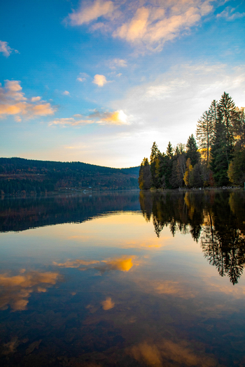 View of a calm lake reflecting a colorful sunset sky and dense evergreen forest on the shore in Breitnau Baden Wurttemberg Germany. View of a calm lake reflecting a colorful sunset sky and dense evergreen forest on the shore in Breitnau Baden Wurttemberg Germany.