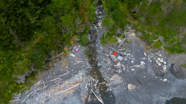 Aerial view of colorful tents pitched among driftwood on a rocky beach near a stream at the Lost Coast in Humboldt County California United States.