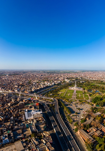 Aerial view of Minar e Pakistan surrounded by lush green gardens urban sprawl and a highway interchange under a clear blue sky in Lahore Punjab Pakistan.