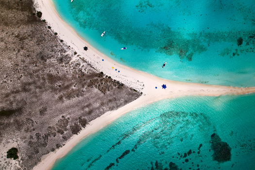 Aerial view of Los Roques archipelago featuring a white sandbar separating turquoise waters with small boats anchored along the shore in Los Roques Dependencias Federale Venezuela. Aerial view of Los Roques archipelago featuring a white sandbar separating turquoise waters with small boats anchored along the shore in Los Roques Dependencias Federale Venezuela.