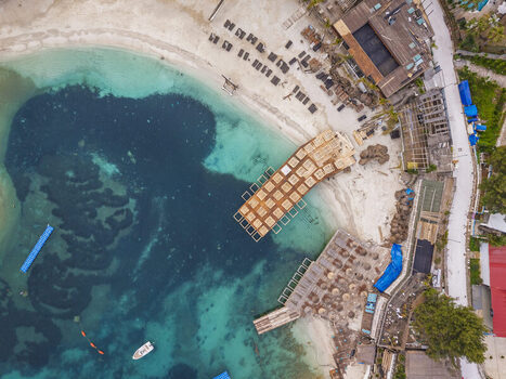 Aerial view of the beach in Ksamil with turquoise waters wooden platforms beach umbrellas and a small boat in Ksamil Vlore County Albania. Aerial view of the beach in Ksamil with turquoise waters wooden platforms beach umbrellas and a small boat in Ksamil Vlore County Albania.