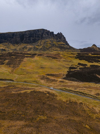Aerial view of The Quiraing featuring rugged cliffs a winding road with a small car and grassy hills under a moody overcast sky Isle of Skye Scotland United Kingdom. Aerial view of The Quiraing featuring rugged cliffs a winding road with a small car and grassy hills under a moody overcast sky Isle of Skye Scotland United Kingdom.