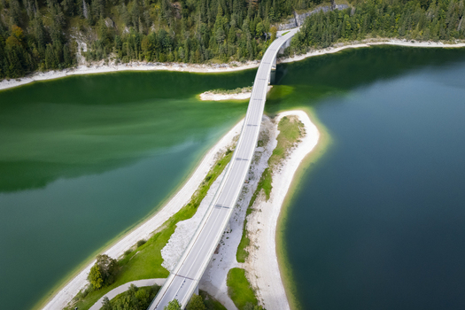 Aerial view of a bridge cutting through the contrasting turquoise and dark blue waters of Sylvensteinspeicher lake framed by lush green forests Sylvensteinspeicher Bavaria Germany. Aerial view of a bridge cutting through the contrasting turquoise and dark blue waters of Sylvensteinspeicher lake framed by lush green forests Sylvensteinspeicher Bavaria Germany.