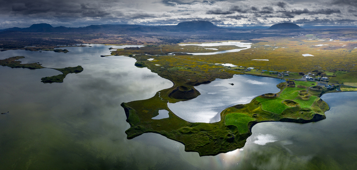 Aerial view of the green pseudocraters of Skutustadagigar at Lake Myvatn with distant mountains under a dramatic cloudy sky Iceland.