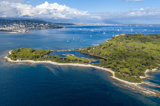 Aerial view of Ile Sainte Marguerite featuring pine forests a central lagoon rocky coastlines and clear blue waters with boats anchored in the bay near Cannes Provence Alpes Cote d Azur France. Aerial view of Ile Sainte Marguerite featuring pine forests a central lagoon rocky coastlines and clear blue waters with boats anchored in the bay near Cannes Provence Alpes Cote d Azur France.