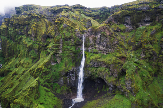 Aerial view of Mulagljufur Canyon with a tall waterfall cascading down steep mossy green cliffs in the Eastern Region Iceland. Aerial view of Mulagljufur Canyon with a tall waterfall cascading down steep mossy green cliffs in the Eastern Region Iceland.