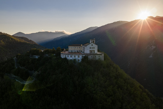 Aerial view of Santuario del Santissimo Salvatore perched on a forested hilltop during sunset with mountains in the background Montella Campania Italy. Aerial view of Santuario del Santissimo Salvatore perched on a forested hilltop during sunset with mountains in the background Montella Campania Italy.