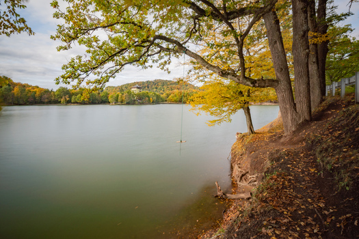 View of Pocuvadlo lake surrounded by vibrant autumn foliage with a rope swing hanging from a tree on the shore in Banska Stiavnica Banskobystricky kraj Slovakia. View of Pocuvadlo lake surrounded by vibrant autumn foliage with a rope swing hanging from a tree on the shore in Banska Stiavnica Banskobystricky kraj Slovakia.