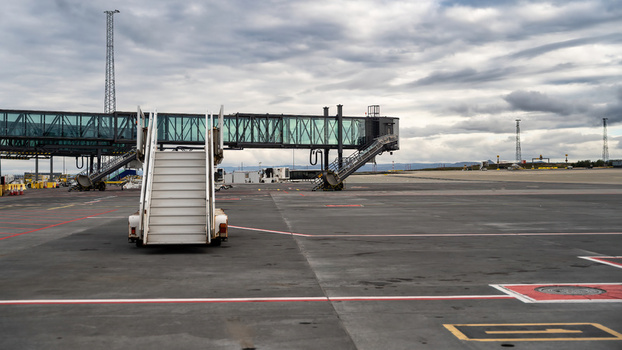 View of a mobile passenger boarding stair on the airport tarmac with jet bridges and a cloudy sky in Iceland.