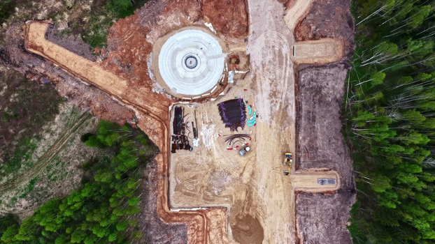 Aerial view of wind turbine foundation under construction with heavy machinery and building materials on a cleared site surrounded by forest in Latvija. Aerial view of wind turbine foundation under construction with heavy machinery and building materials on a cleared site surrounded by forest in Latvija.