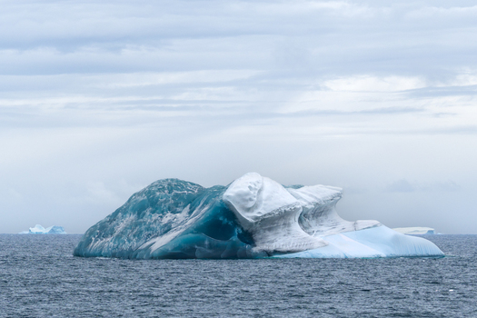 View of a large iceberg with deep blue ice and white snow formations floating in the Southern Ocean near the South Orkney Islands. View of a large iceberg with deep blue ice and white snow formations floating in the Southern Ocean near the South Orkney Islands.