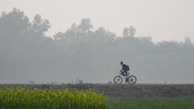 View of a person riding a bicycle through a foggy field Bangladesh. View of a person riding a bicycle through a foggy field Bangladesh.