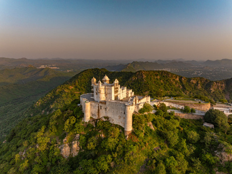 Aerial view of the historic Sajjangarh Palace also known as the Monsoon Palace perched atop a lush green hill overlooking the surrounding Aravalli mountains in Udaipur Rajasthan India.